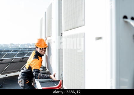 Professional operaio in abbigliamento protettivo Installazione unità esterna di un condizionatore d'aria o pompa di calore sul tetto Foto Stock
