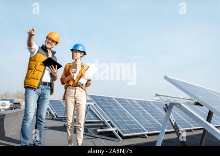 Due ingegneri o architetti esaminando la costruzione di una centrale solare, passeggiate con tavoletta digitale su un tetto Foto Stock