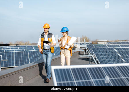 Due ingegneri o architetti esaminando la costruzione di una centrale solare, passeggiate con tavoletta digitale su un tetto Foto Stock