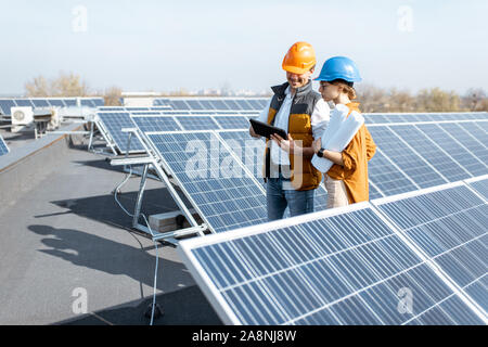 Due ingegneri o architetti esaminando la costruzione di una centrale solare, passeggiate con tavoletta digitale su un tetto Foto Stock