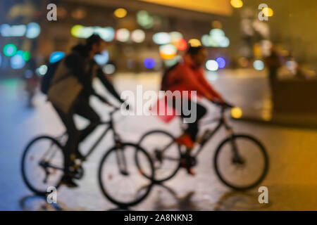 Sagome di astratta irriconoscibile coppia giovane, equitazione biciclette, night city, illuminazione bokeh, motion blur. Uno stile di vita sano, le attività per il tempo libero Foto Stock