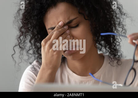 Infelice americano africano donna prendendo il largo bicchieri, sensazione di affaticamento della vista Foto Stock