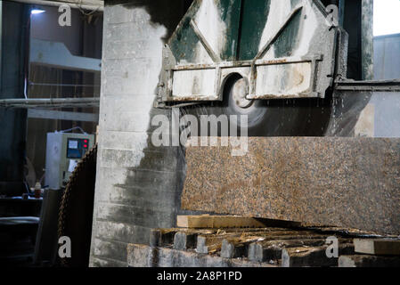 Elaborazione di granito in produzione. Il taglio di lastre di granito con una sega circolare. Utilizzo di acqua per il raffreddamento. Segatura industriale del granito Foto Stock