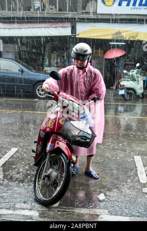 Biker su scooter motociclo attraverso strade allagate durante temporali,Thailandia Foto Stock