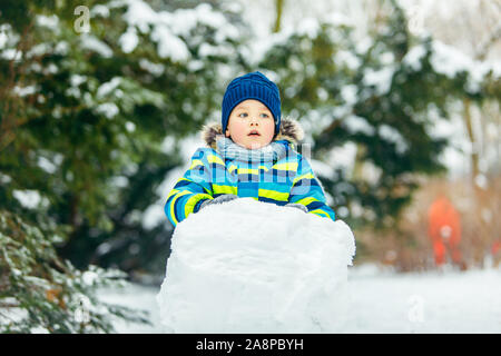 Poco carino boy rendendo pupazzo di neve. il rotolamento grande palla di neve Foto Stock