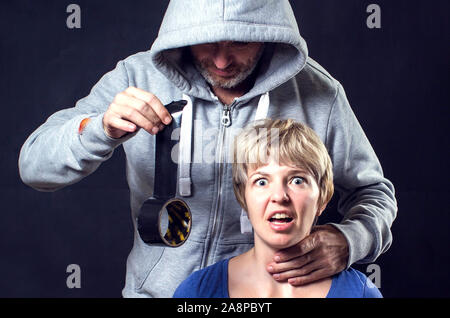 Uomo in felpa con cappuccio che copre una donna'sla bocca con dello scotch. Concetto di violenza o di sequestro. Foto Stock