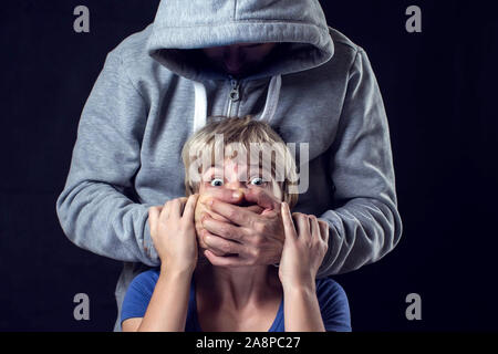 Uomo in felpa con cappuccio che copre una donna'sbocca. Concetto di violenza o di sequestro. Foto Stock