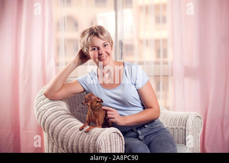 Donna peccato con piccolo cane giocattolo terrier sulla poltrona. Persone e animali concept Foto Stock