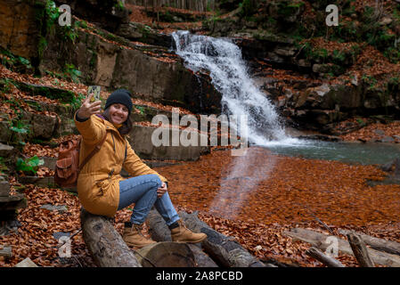 Donna seduta sul log guardando a cascata la stagione autunnale Foto Stock