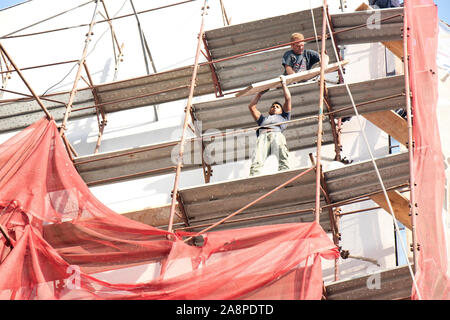 A Belgrado, in Serbia - Ottobre 25, 2019: due sprotetto lavoratori edili sul patibolo durante la facciata del palazzo la ricostruzione, un pericoloso, un pericolo Foto Stock