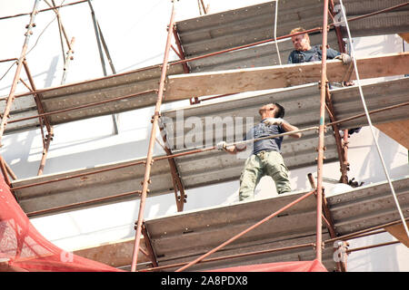 A Belgrado, in Serbia - Ottobre 25, 2019: due sprotetto lavoratori edili sul patibolo durante la facciata del palazzo la ricostruzione, un pericoloso, un pericolo Foto Stock