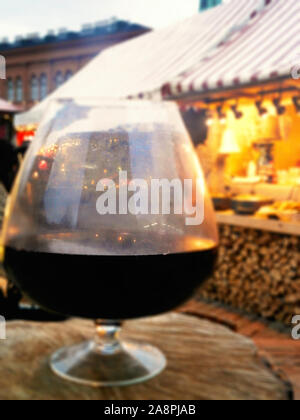 Grande bicchiere di vino con una riflessione sfocata delle luci di festa nella piazza del paese, festa di Natale, città mercato, outdoor cafe bar o con i prodotti alimentari Foto Stock