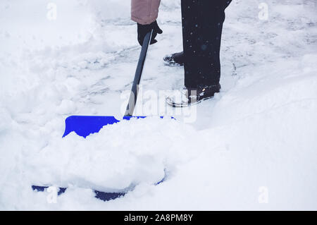 Le mani di un uomo che pulisce la neve sulla strada dopo una bufera di neve. Pulire le strade della città dopo la nevicata. Foto Stock