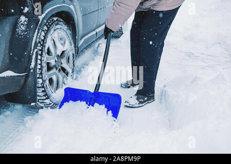 Le mani di un uomo che pulisce la vettura e rimuove la neve sulla strada dopo una tempesta di neve. Pulire le strade della città dopo la nevicata. Foto Stock