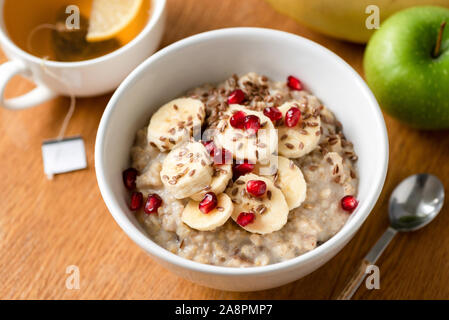 Il Porridge di avena o farina di avena nella ciotola con banana slice, i semi di melograno e semi di lino su una tavola di legno dello sfondo. Messa a fuoco selettiva. Una sana prima colazione, Foto Stock