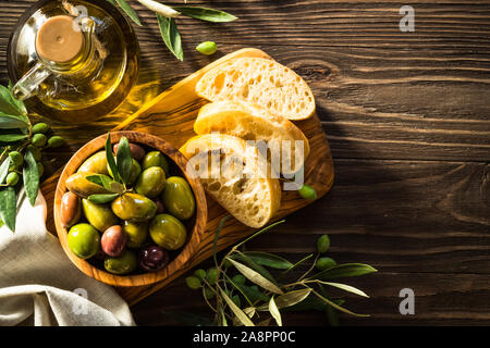 Olive e olio d'oliva e ciabatta sul tavolo di legno. Foto Stock