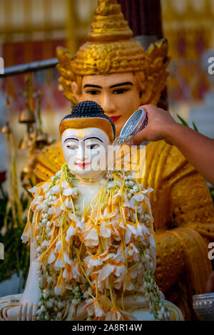 Stretta di mano versando acqua sulla statua di Buddha a Yangon, Myanmar. Shwedagon pagoda. Foto Stock