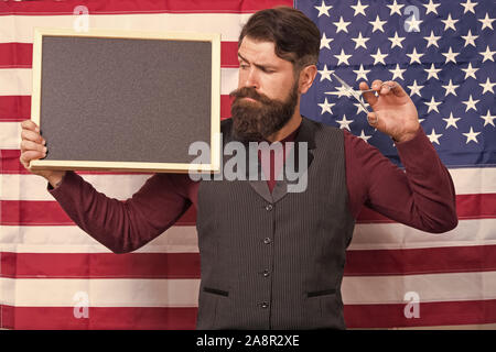 Educazione patriottica. Uomo Barbuto holding forbici e Blackboard nella scuola di educazione. Barbiere corsi di istruzione. Hipster dando lezione sulla bandiera americana sfondo. Istruzione e carriera, copia dello spazio. Foto Stock