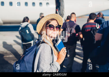 Donna traveler imbarco sul piano tenendo il passaporto. Felice passeggero con zaino in piedi in linea pronto per il volo Foto Stock