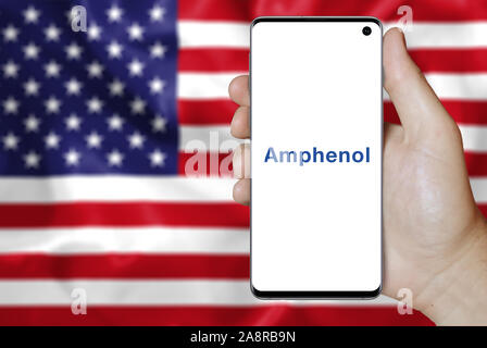 Il logo della società pubblica Amphenol Corp visualizzato su uno smartphone. Bandiera degli Stati Uniti sullo sfondo. Credito: PIXDUCE Foto Stock
