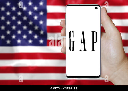 Il logo della società pubblica Gap Inc. visualizzata su uno smartphone. Bandiera degli Stati Uniti sullo sfondo. Credito: PIXDUCE Foto Stock