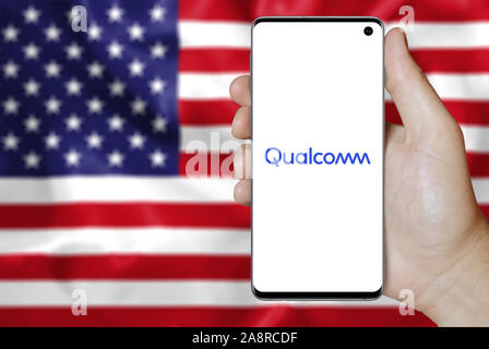 Il logo della società pubblica Qualcomm Inc. visualizzata su uno smartphone. Bandiera degli Stati Uniti sullo sfondo. Credito: PIXDUCE Foto Stock