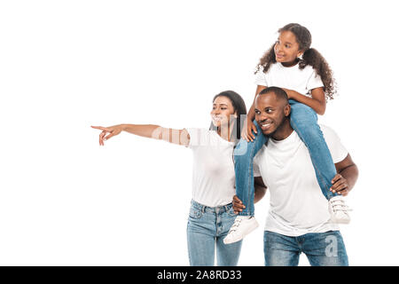 Allegro americano africano donna puntando con il dito e il marito piggybacking adorabile figlia isolato su bianco Foto Stock