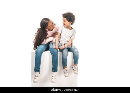 Carino African American sorella guardando adorabili fratello mentre è seduto sul cubo bianco insieme isolato su bianco Foto Stock