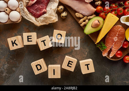 Vista superiore della carne cruda e pesce nei pressi di uova, formaggio, pomodori e avocado e arachidi sulla superficie di marmo con cubetti di legno dieta cheto iscrizione Foto Stock