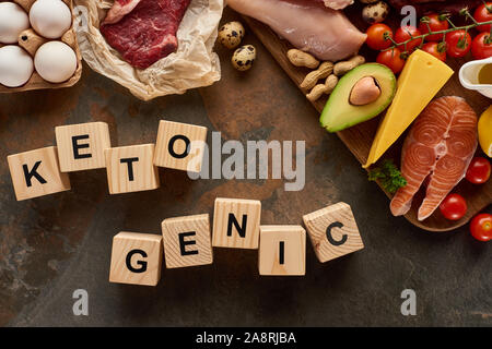 Vista superiore della carne cruda e pesce nei pressi di uova, formaggio, pomodori e avocado e arachidi sulla superficie di marmo con cubetti di legno ketogenic iscrizione Foto Stock