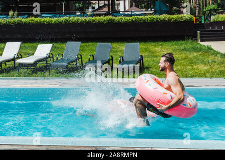 Vista laterale dell'uomo con anello gonfiabile jumping in piscina Foto Stock