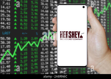 Il logo della società pubblica la Hershey Company visualizzata su uno smartphone. Positivo del mercato azionario sfondo. Credito: PIXDUCE Foto Stock