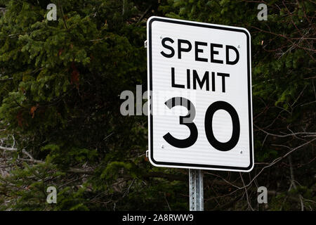 Un bianco velocità limite 30 miglia per ora firmare con un verde scuro albero sempreverde sfondo su una strada in speculatore, NY USA Foto Stock