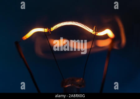 Filamento luminoso della lampada ad incandescenza close-up su uno sfondo blu scuro Foto Stock