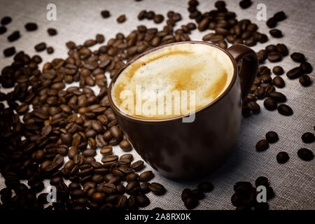 Una tazza di caffè fresco con schiuma sulla tabella prevista dalla tela e sparse in grani di caffè Foto Stock