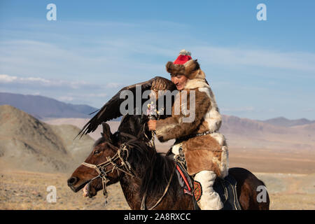 Tradizionale aquila kazaka hunter alimentando il suo golden eagle a cavallo. Ulgii, Mongolia. Foto Stock