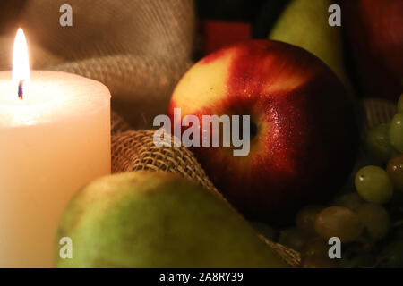 Red apple con gocce di acqua e candela luce morbida. Close up. Autunno still life con frutti su un letto di sacco sullo sfondo Foto Stock