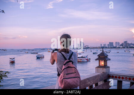 Pattaya, Tailandia - 19 Aprile 2019: bella donna prendendo una foto del tramonto. Felice giovane donna con una macchina fotografica e uno zaino. Foto Stock