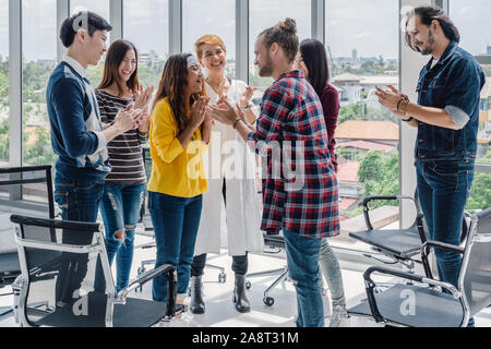 Senior manager creativo uomo dando il nuovo circa il promuovere la posizione alla asian junior donna lavoratrice nel centro del gruppo di asiatici e multietnica Bu Foto Stock