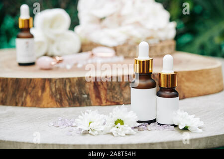 Bottiglie piccole con sieri e essenze sul tavolo di legno con petali di fiori e gemme preziose Foto Stock