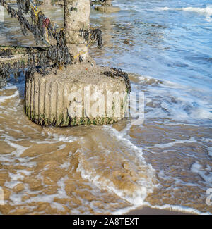 Dolci onde che lambiscono il calcestruzzo al piede di un molo sulla costa di Norfolk Foto Stock