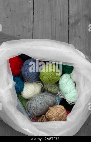 Palle di filati di lana in una selezione di colori e stili in una borsa bianca. Pavimento in legno sfondo con colore selettivo Foto Stock