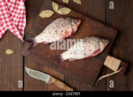 Fresco pesce carassio cosparso con spezie giace su un marrone tagliere in legno, tavolo in legno da schede, vista dall'alto Foto Stock