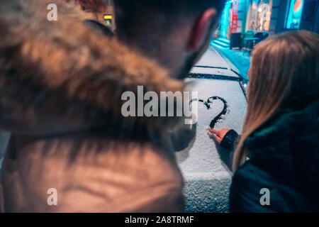 Giovane adulto giovane disegna un cuore sulla neve auto coperto, Chiudi vista Foto Stock