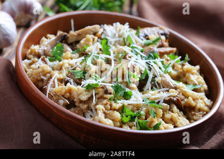Stile rustico di funghi selvatici cremoso risotto con parmigiano grattugiato in un recipiente di terracotta, vista da sopra, close-up Foto Stock