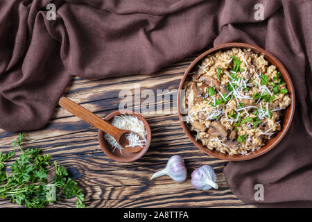 Stile rustico di funghi selvatici cremoso risotto con parmigiano grattugiato in un recipiente di terracotta, vista da sopra, flatlay Foto Stock