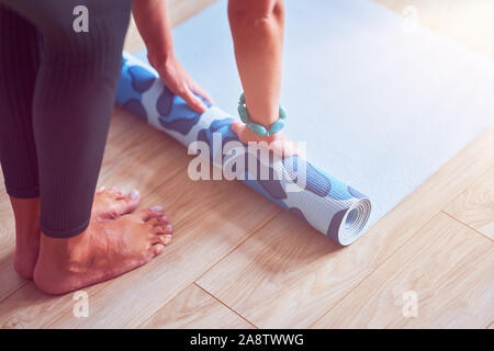 Giovane donna rolling materassino yoga a casa Foto Stock