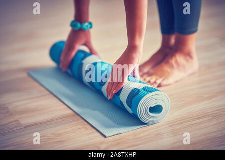 Giovane donna rolling materassino yoga a casa Foto Stock