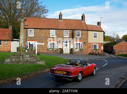 Senior uomo alla guida di red Triumph Spitfire auto sportiva nel villaggio di Lund, East Yorkshire, Inghilterra, Regno Unito Foto Stock