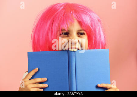 Ragazza morde Big Blue Book. Pupilla in uniforme scolastica con parrucca rosa. School girl isolato su sfondo rosa. Si torna a scuola e istruzione concetto. Foto Stock